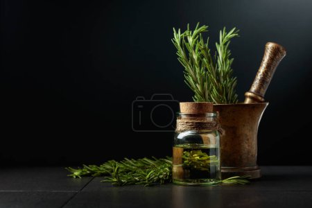 Photo for Bottle of rosemary aromatherapy oil extract with fresh rosemary branches and old brass mortar. Black background with copy space. - Royalty Free Image