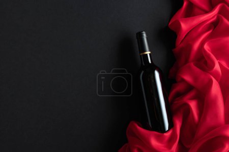 Foto de Bottle of red wine with red satin on a black background. Top view. - Imagen libre de derechos