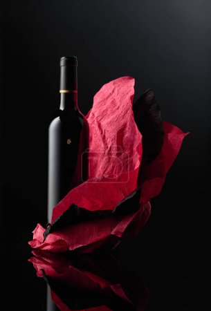 Téléchargez les photos : Une bouteille de vin rouge sur un papier froissé. Fond réfléchissant noir. - en image libre de droit