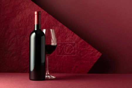 Photo for Bottle and glass of red wine on a red background. Copy space for your text. - Royalty Free Image