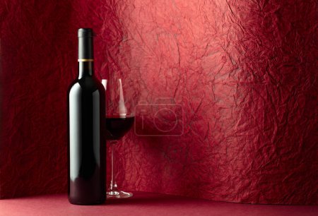 Téléchargez les photos : Bouteille et verre de vin rouge sur fond rouge. Copiez l'espace pour votre texte. - en image libre de droit