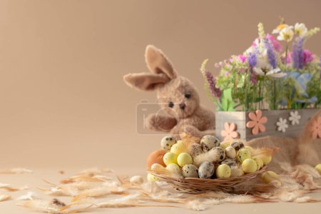 Photo for Easter eggs, feathers, spring flowers, and toy bunny on a beige background. Focus on a foreground. - Royalty Free Image