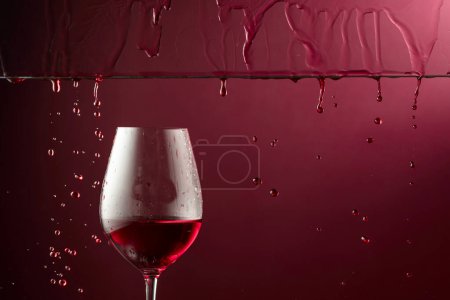 Foto de El vino tinto fluye hacia abajo en una copa. Fondo rojo oscuro con espacio de copia. - Imagen libre de derechos