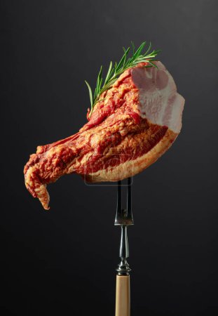 Stück geräuchertes Schweinefleisch mit Rosmarin auf einer Gabel.