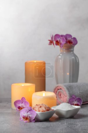 Téléchargez les photos : Sel marin, serviettes, fleurs d'orchidées et bougies allumées sur fond gris. Concept de spa avec espace de copie. - en image libre de droit