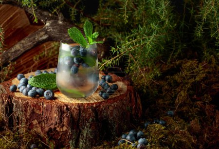 Photo for Cocktail with ice, blueberries, and mint on a pine stump in the forest. Summer fresh fruit drink. - Royalty Free Image