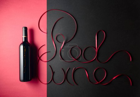 Téléchargez les photos : Bouteille de vin rouge avec rubans de satin rouge. Ruban de satin mince en forme de mots Vin rouge. Espace de copie. - en image libre de droit