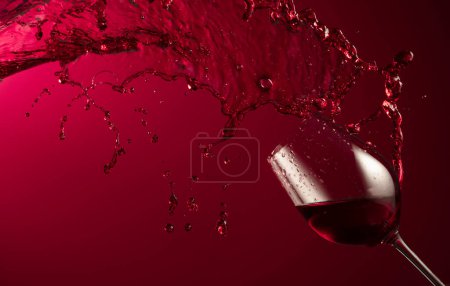 Foto de Salpicadura de vidrio y vino tinto sobre un fondo rojo oscuro. Copiar espacio. - Imagen libre de derechos
