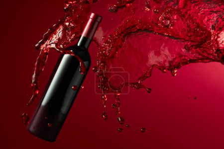 Foto de Botella de vino tinto y salpicadura sobre fondo rojo oscuro. Copiar espacio. - Imagen libre de derechos