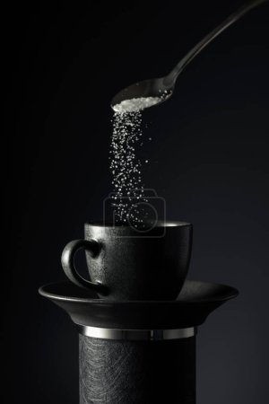 Foto de Una taza de café negro sobre un fondo negro. El azúcar se vierte en una taza de café. Copiar espacio. - Imagen libre de derechos