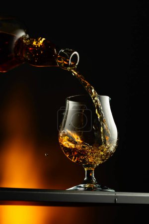 Téléchargez les photos : Cognac ou brandy versé dans un verre. Brandy snifter sur un fond sombre. - en image libre de droit