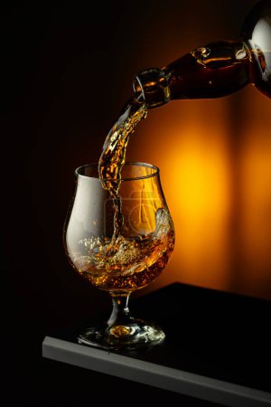Photo for Cognac or brandy being poured into a glass. Brandy snifter on a dark background. - Royalty Free Image
