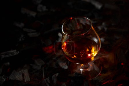 Foto de Snifter de brandy en un carbón quemado. Concepto de bebidas alcohólicas duras. Copiar espacio. - Imagen libre de derechos