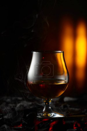 Foto de Snifter de brandy en un carbón quemado. Concepto de bebidas alcohólicas duras. Copiar espacio. - Imagen libre de derechos