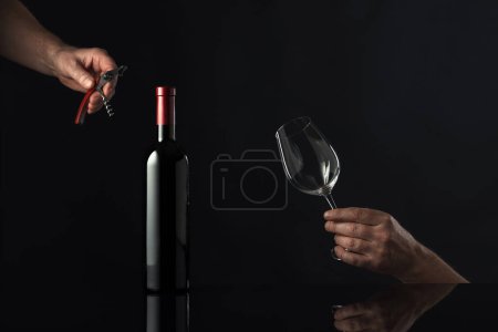 Photo for Unopened bottle of red wine and hands with corkscrew and wine glass. Concept of the wine theme. Copy space. - Royalty Free Image