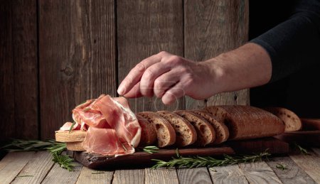 Photo for Prosciutto with bread and rosemary on an old wooden table. Traditional Mediterranean food. - Royalty Free Image