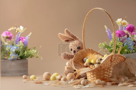 Foto de Huevos de Pascua, plumas, flores de primavera y conejito de juguete sobre un fondo beige. Concéntrate en un primer plano. - Imagen libre de derechos