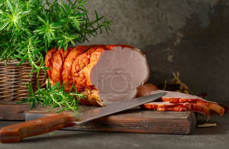 Photo for Tasty smoked pork ham with rosemary, onion, garlic, red pepper, and bay leaves. Smoked meat on a kitchen table. - Royalty Free Image