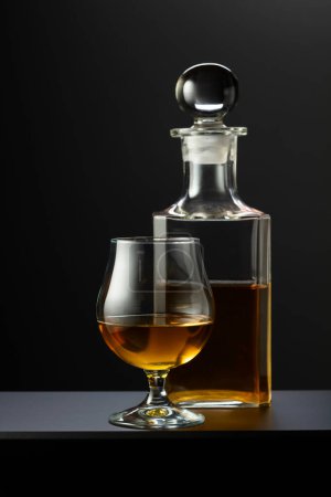 Téléchargez les photos : Vieux carafe et verre avec whisky, cognac ou brandy sur fond noir. - en image libre de droit