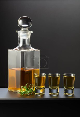 Téléchargez les photos : Vieille carafe, verres avec boisson alcoolisée forte et brindille de romarin sur fond noir. - en image libre de droit
