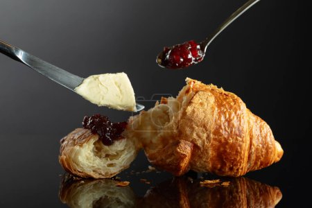 Foto de Croissant recién horneado con mermelada de mantequilla y frambuesa sobre un fondo negro reflectante. - Imagen libre de derechos
