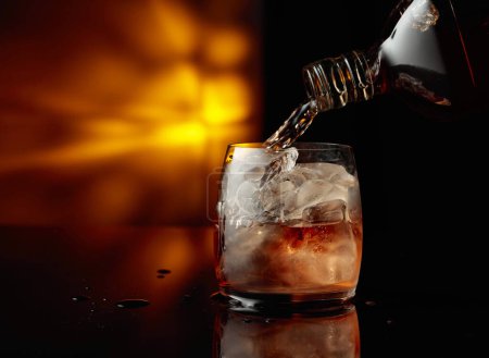 Photo for Pouring whiskey from a bottle into a glass with ice. Copy space. - Royalty Free Image