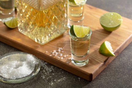 Téléchargez les photos : Tequila d'or avec sel de mer et tranches de citron vert sur une planche à découper. - en image libre de droit