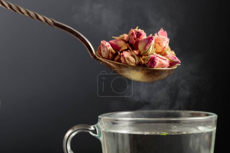 Foto de Brotes de rosa secos para hacer té de hierbas y taza con agua caliente. - Imagen libre de derechos
