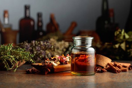 Photo for Essential herbal tincture in a small glass bottle. On a table dried herbs, flowers, spices, and old kitchen utensils. Alternative or complementary medicine treatment. - Royalty Free Image