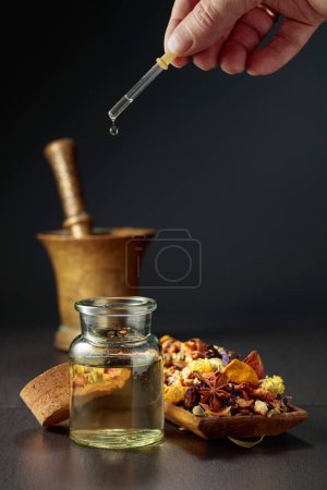 Photo for Dropping essential oil or herbal tincture into a glass bottle. Mix of dried healthy medicinal herbs and healing plants on a black background. Copy space. - Royalty Free Image