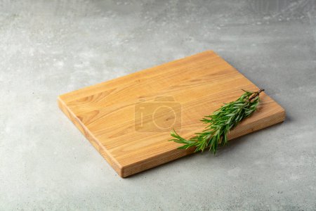 Téléchargez les photos : Planche à découper et romarin sur une table en pierre. Fond culinaire. Planche à découper en bois vide, espace d'affichage des produits. - en image libre de droit