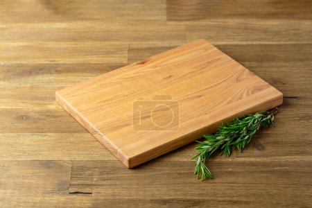 Photo for Cutting board and rosemary on an old wooden table. Culinary background. Empty wooden cutting board, product display space. - Royalty Free Image