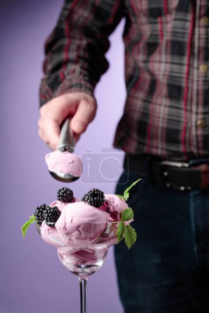 Foto de Helado de mora con bayas. El hombre pone helado en una taza de helado
. - Imagen libre de derechos