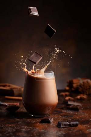 Foto de Pedazos de chocolate negro caen en un vaso de bebida de cacao creando un hermoso chapoteo. - Imagen libre de derechos