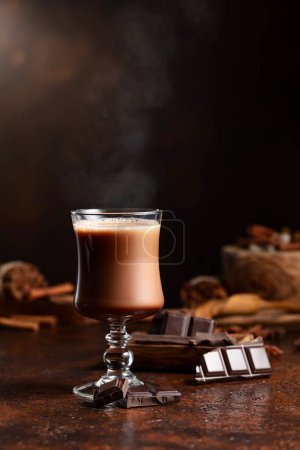 Photo for Glass of cocoa drink and pieces of dark chocolate on a brown vintage table. - Royalty Free Image