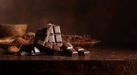 Photo for Broken dark chocolate bar and cocoa powder on a brown table. Copy space. - Royalty Free Image