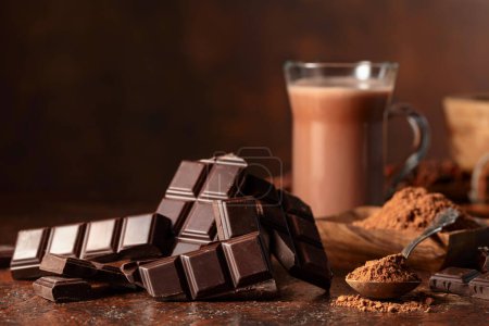 Foto de Pedazos de chocolate amargo y vaso de bebida de cacao en una mesa vintage marrón. Copiar espacio. - Imagen libre de derechos