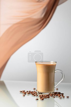 Téléchargez les photos : Café à la crème sur une table en verre. En arrière-plan ondulant rideau beige. - en image libre de droit