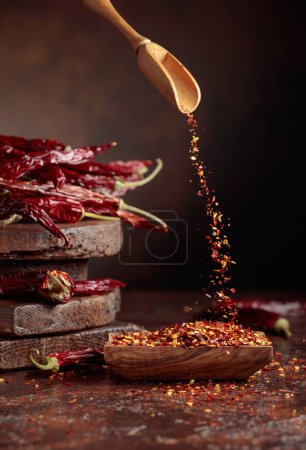 Photo for Chilli flakes are poured into a wooden dish. Chilli flakes and dried chili peppers on a brown background. - Royalty Free Image