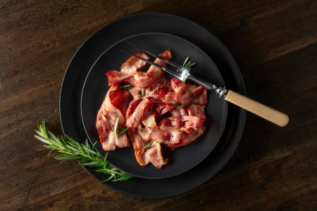 Photo for Roasted bacon slices with rosemary on an  old wooden table. Copy space. Top view. - Royalty Free Image