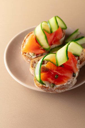 Photo for Sandwiches with smoked trout, cream cheese, fresh cucumber and capers on a beige plate. Copy space. - Royalty Free Image