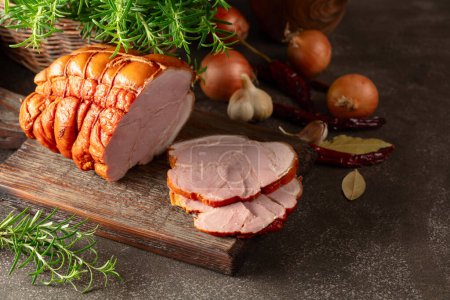 Savoureux jambon de porc fumé avec romarin, oignon, ail, poivron rouge et feuilles de laurier. Viande fumée sur une table de cuisine.