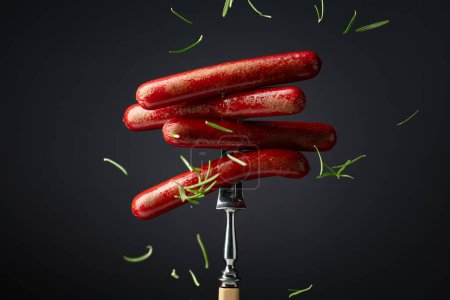 Téléchargez les photos : Saucisses grillées sur une fourchette saupoudrée de romarin. - en image libre de droit