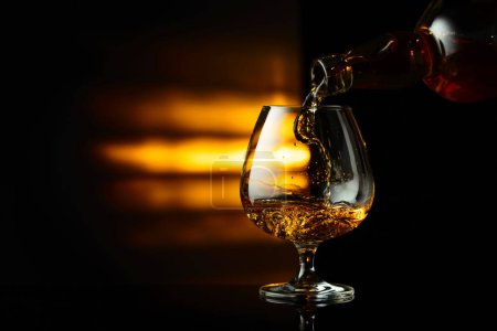 Foto de Verter el brandy de una botella en un snifter sobre un fondo reflectante negro. Copiar espacio. - Imagen libre de derechos