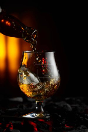Photo for Cognac or brandy being poured into a glass. Snifter on a burning charcoal. Concept of hard alcoholic drinks. - Royalty Free Image
