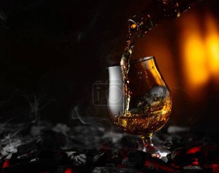 Photo for Cognac or brandy being poured into a glass. Snifter on a burning charcoal. Concept of hard alcoholic drinks. - Royalty Free Image