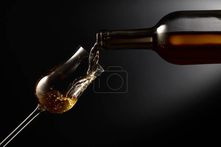 Téléchargez les photos : Glass of premium alcohol on a black background. The drink is poured from a bottle into a glass. Copy space. - en image libre de droit