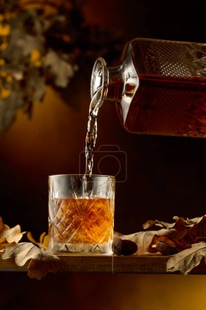 Photo for Whiskey is poured into a frozen glass with ice. - Royalty Free Image