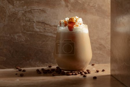 Photo for Iced caramel latte topped with whipped cream and caramel sauce, refreshing and sweet coffee drink on a beige ceramic table. - Royalty Free Image