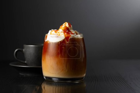 Photo for Iced coffee with whipped cream and caramel sauce and cup of black coffee on a black wooden table. Copy space. - Royalty Free Image